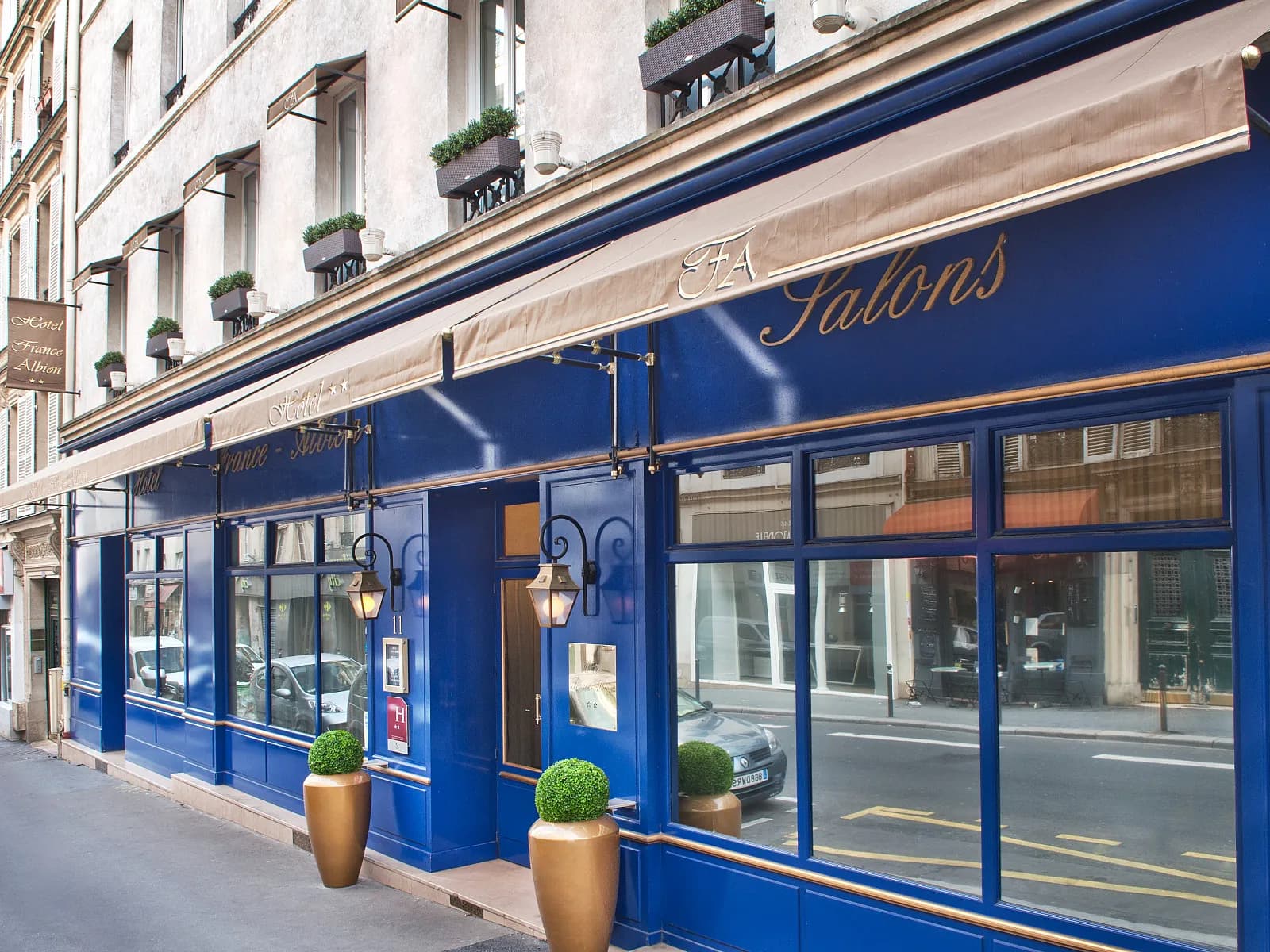 Street facade of Hôtel France Albion in Paris's 9th arrondissement, with a blue frontage and a striped awning