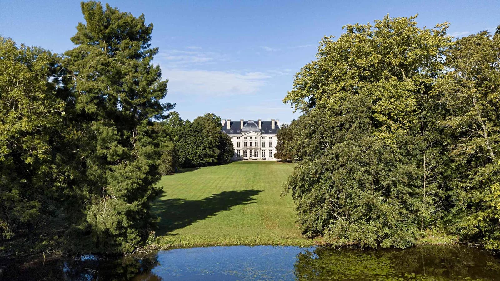 Château with lawns and a pond framed by trees at Manoir des Vallées Claires, Eure-et-Loir