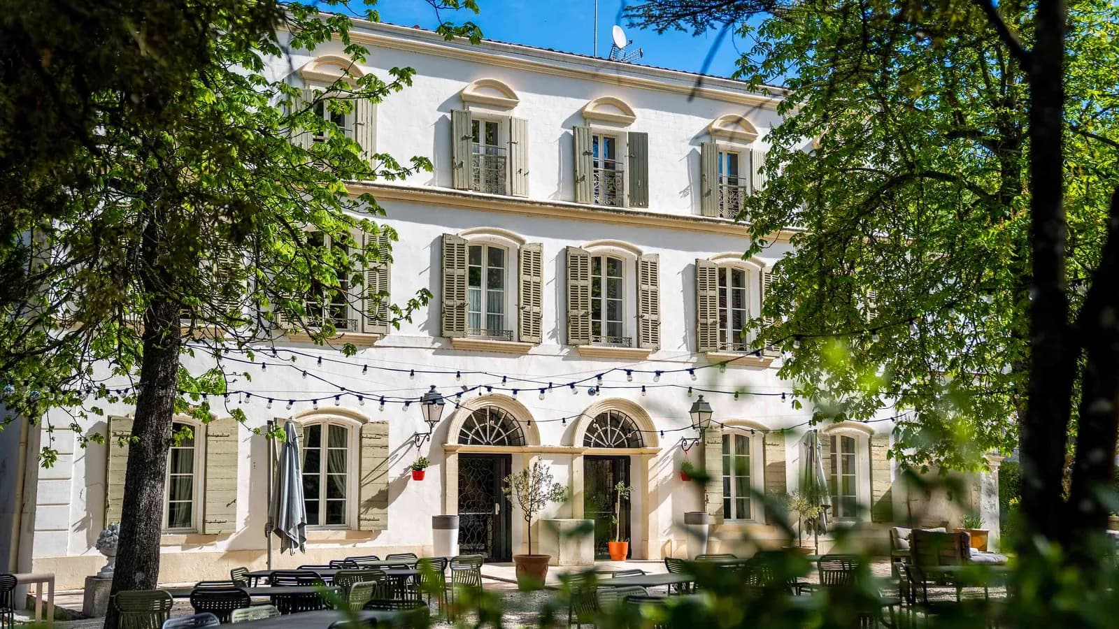 White Provençal bastide with green shutters and tall trees at Bastide des Collines Dorées, Var