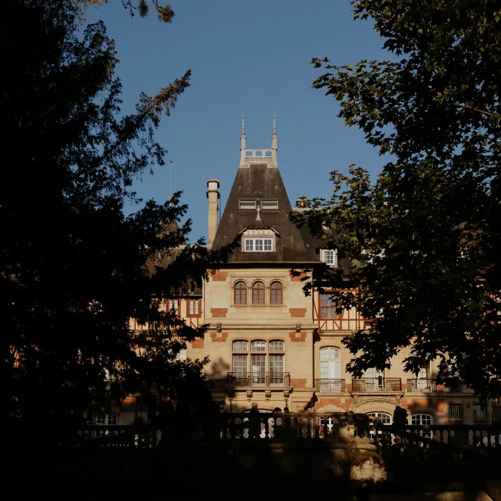 Château Jeanne & The Forest through the trees, its ornate brick and stone façade and pointed roofs in the Chantilly forest