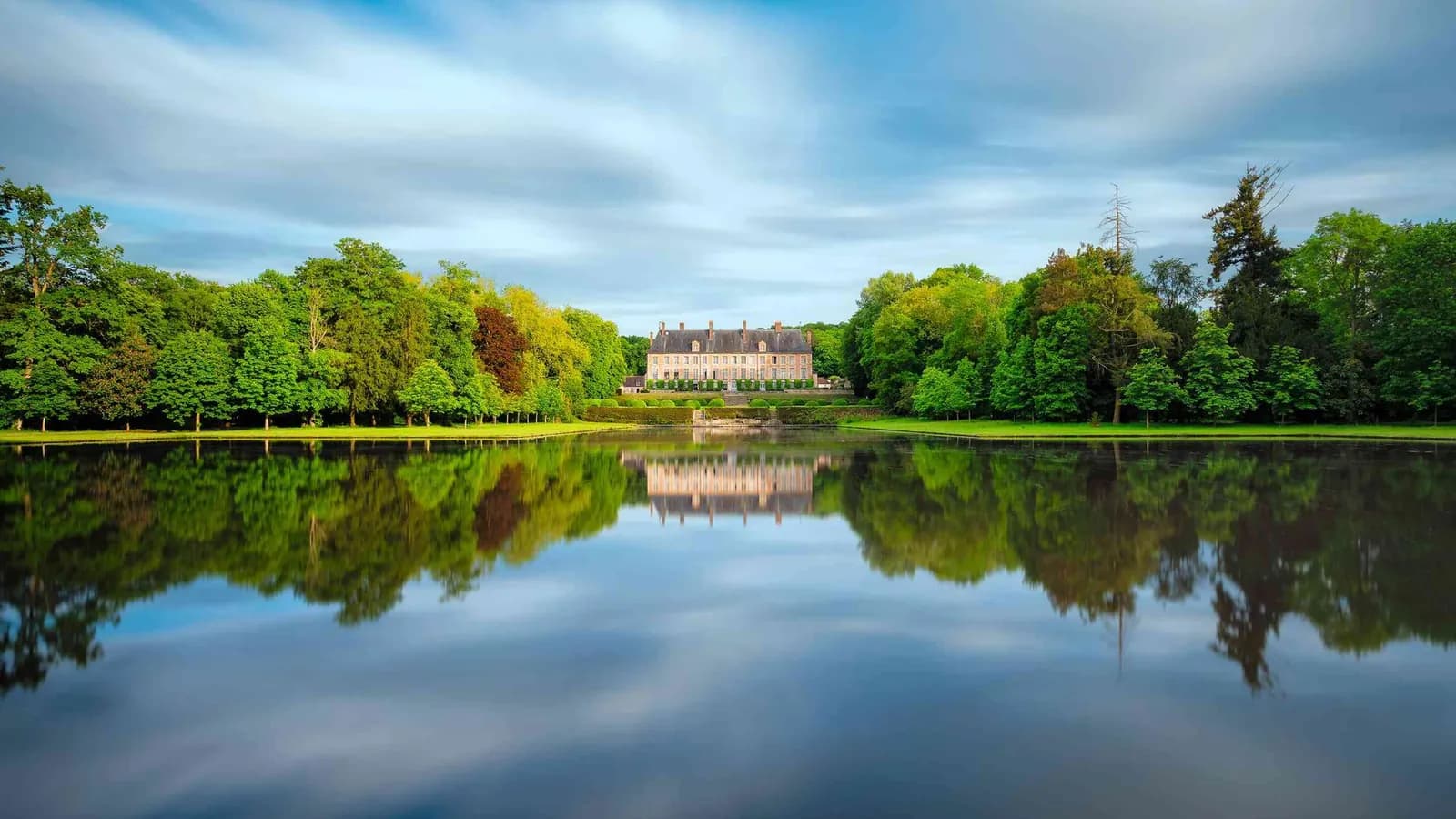 Château reflected in a still lake under a cloudy sky at Château des Grandes Perspectives, Yvelines