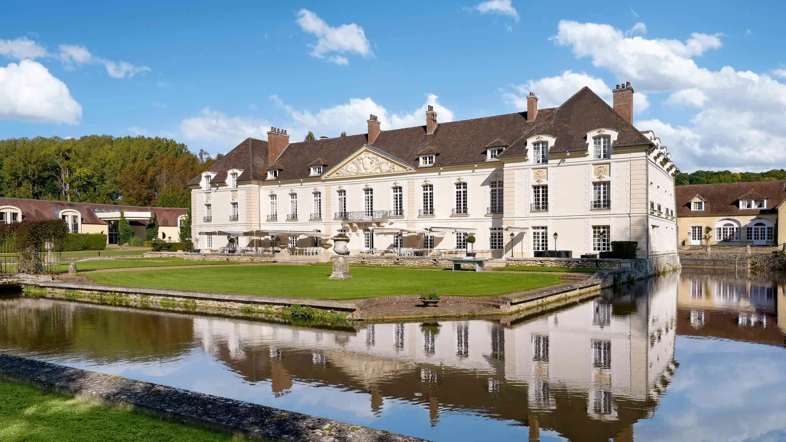 Château reflected in a long pond with woodland and lawns at Château des Hauts Tilleuls, north of Paris