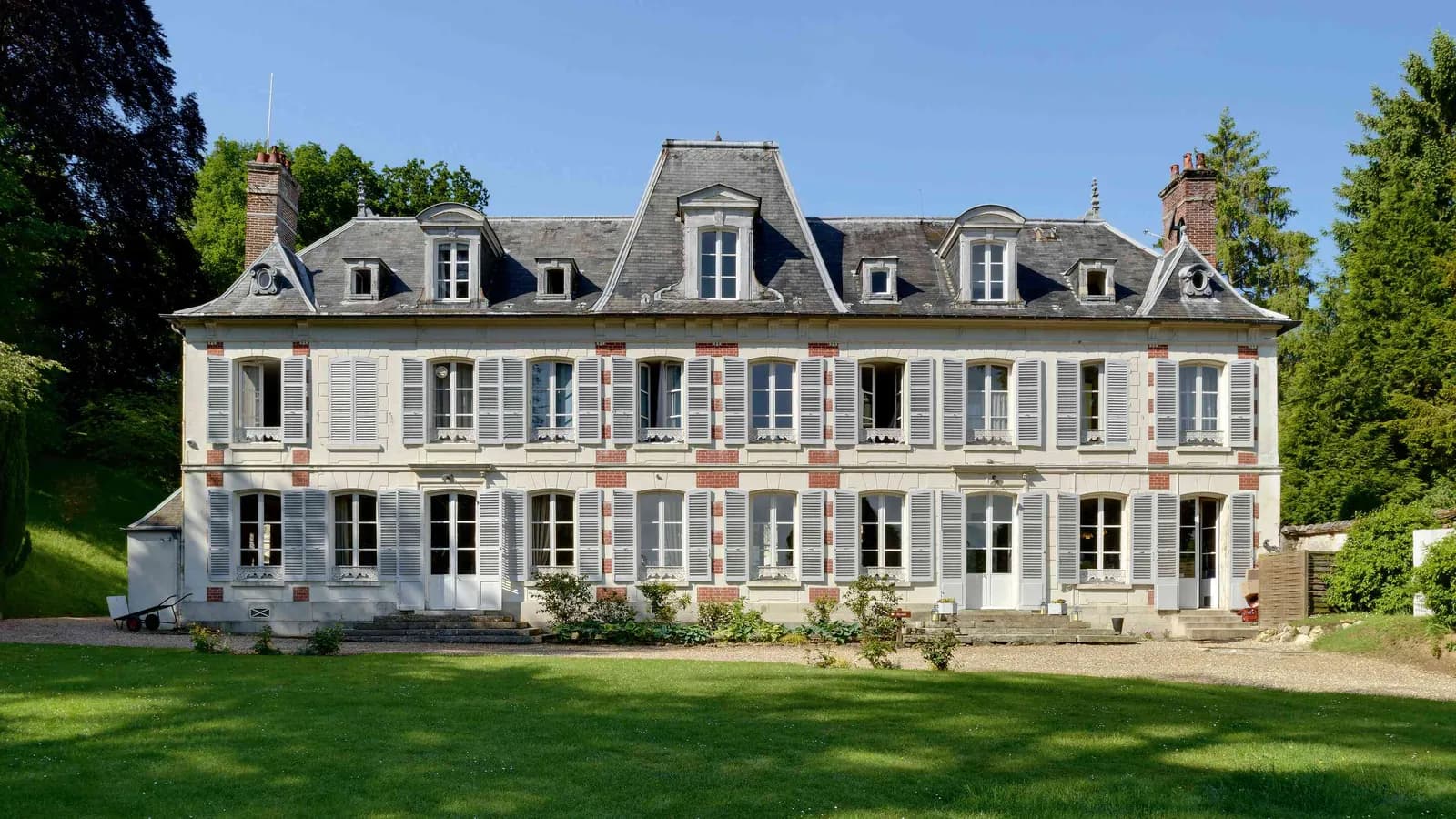 Grey-stone château facade with dormer windows and a sweeping lawn at Château des Lauriers Champêtres, Eure