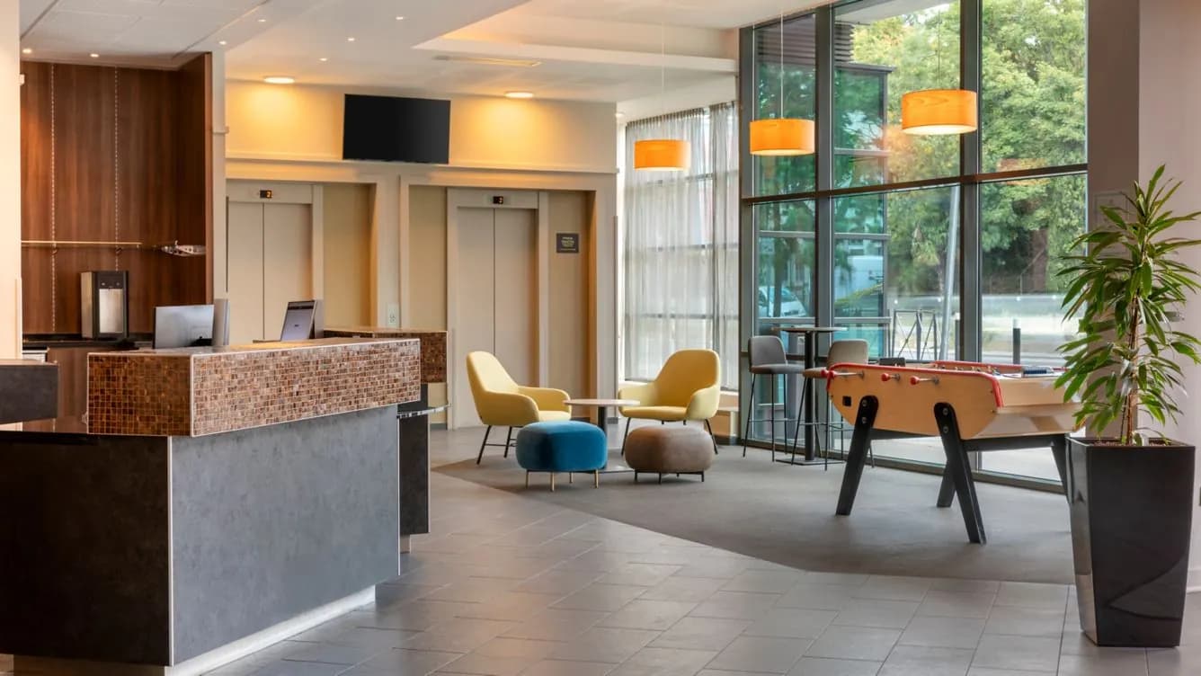 Lobby with reception desk, yellow lounge chairs and table football at Courtyard Paris Saint-Denis
