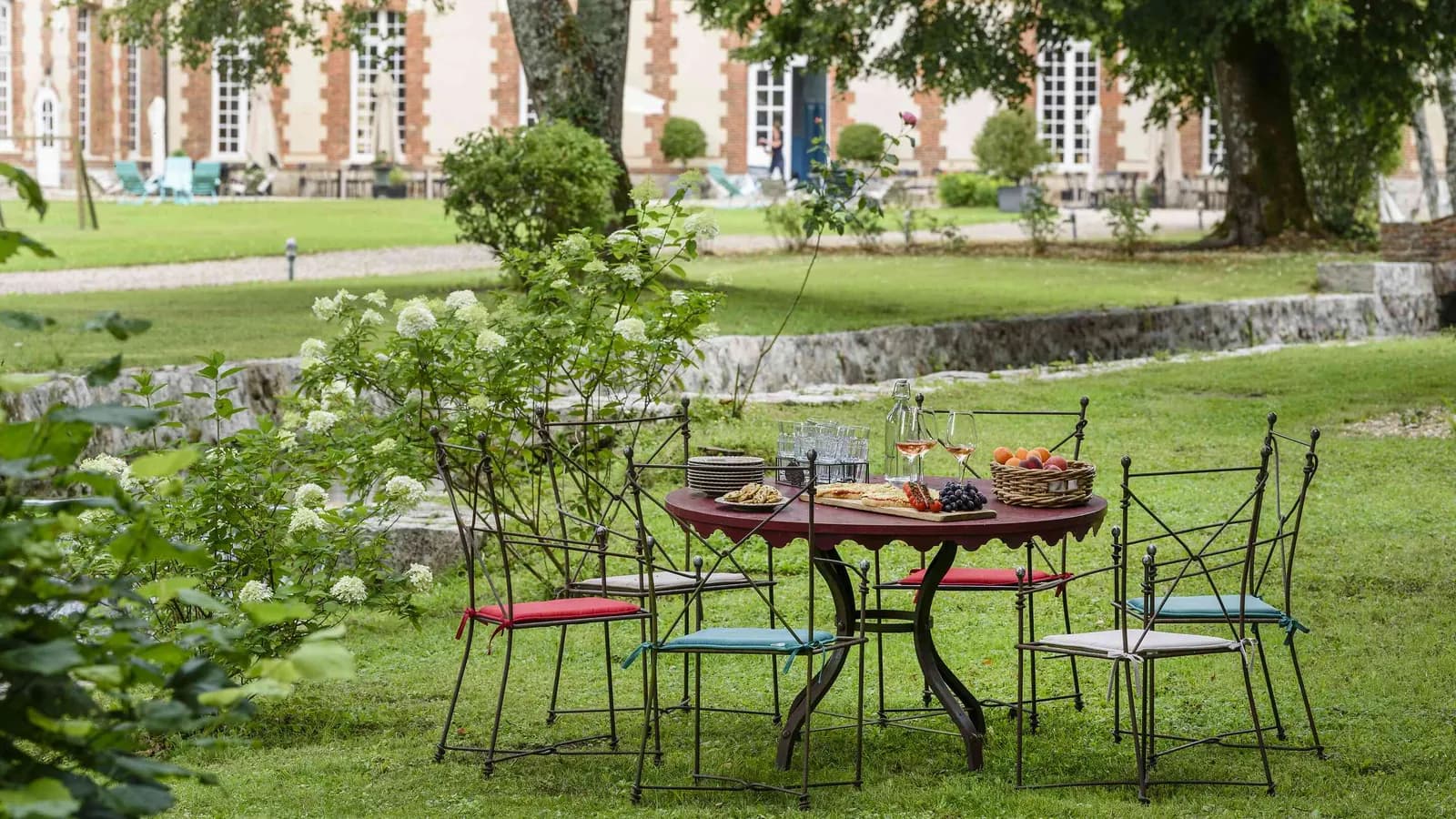 Garden terrace with wrought-iron table and chairs beside the brick manor of Demeure des Pommiers Roses