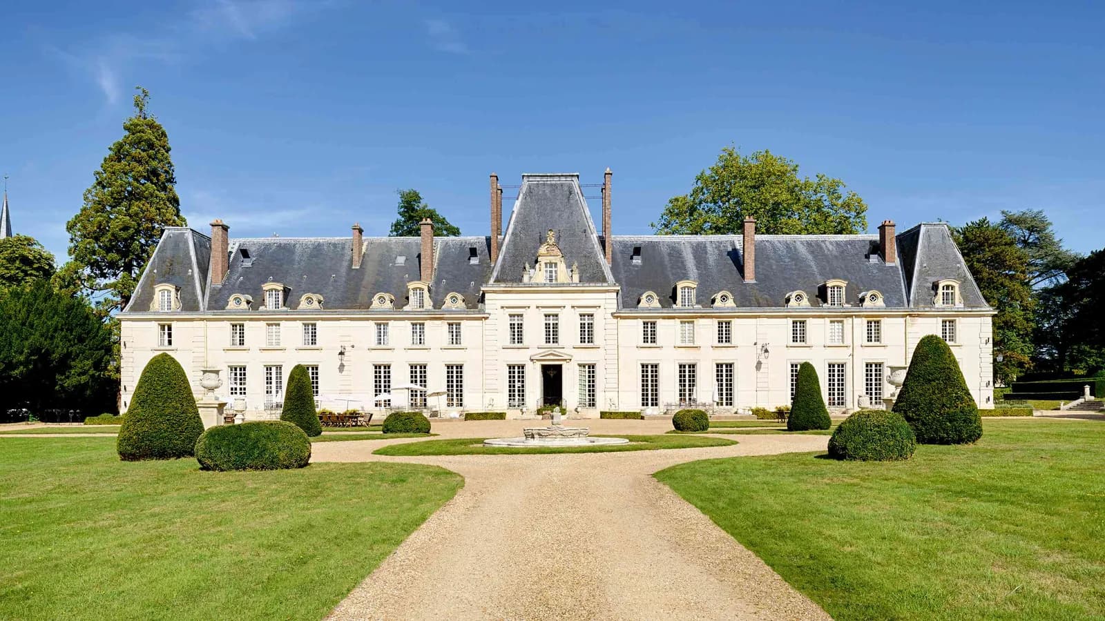 Château facade on a manicured lawn with clipped topiary at Domaine de la Cour Verte, west of Paris
