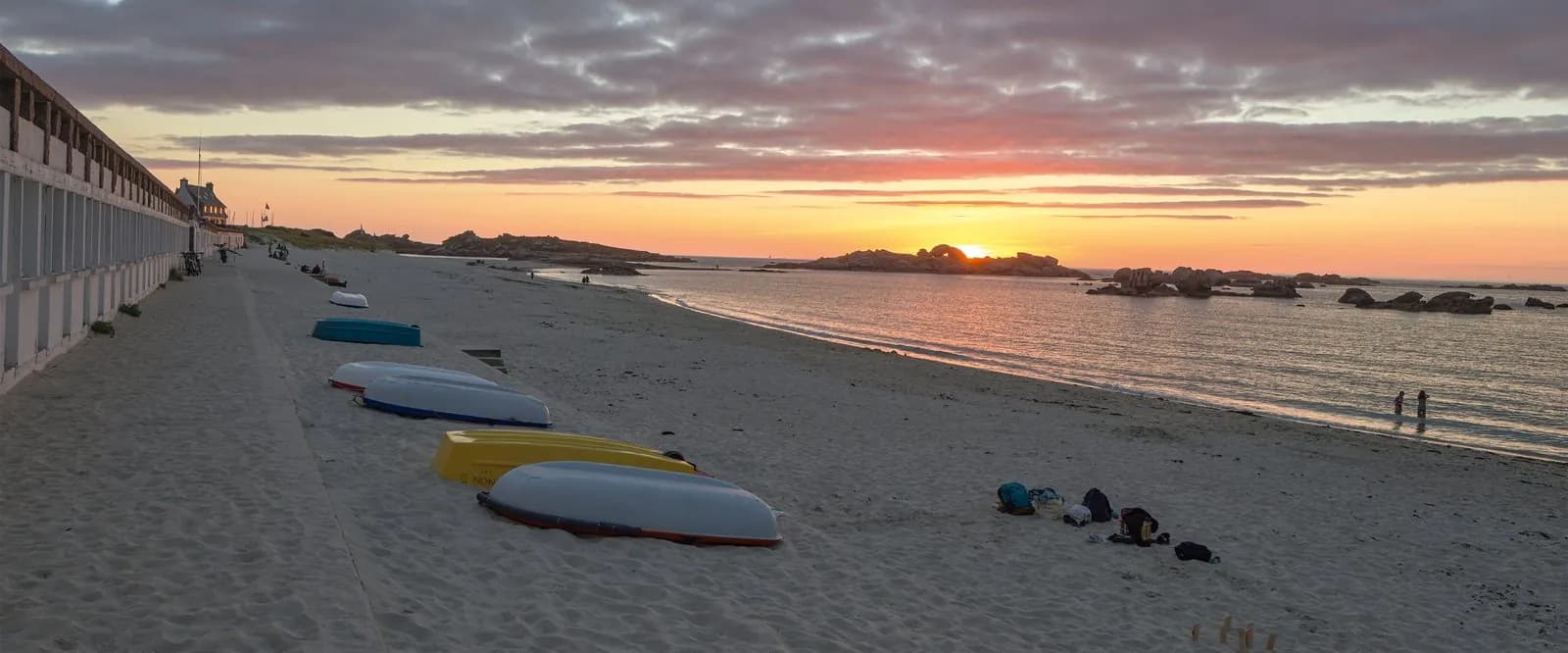 Sandy beach at sunset with kayaks on the sand and rocky islets offshore at Domaine des Embruns, Brittany