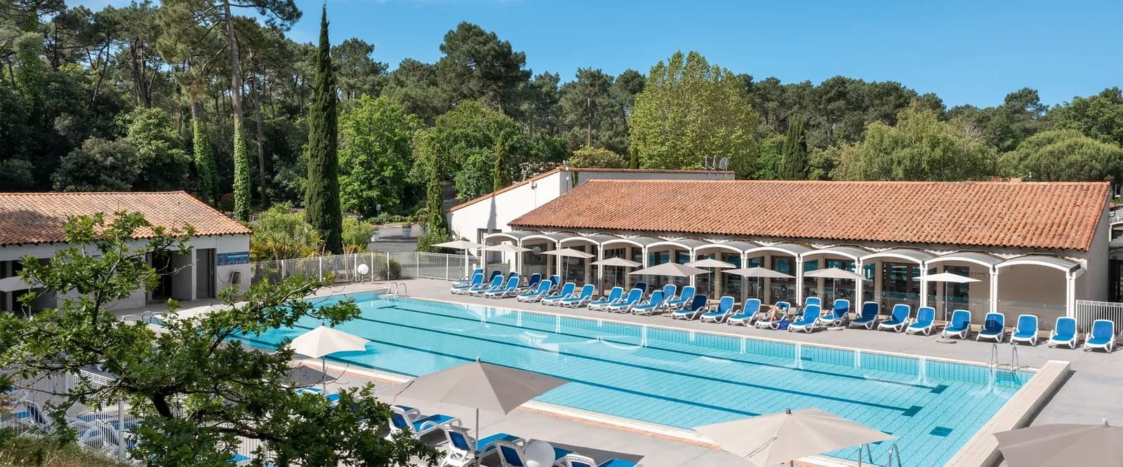 Outdoor pool beside terracotta-roofed pavilions and tall pine trees at Domaine des Pinèdes Atlantiques