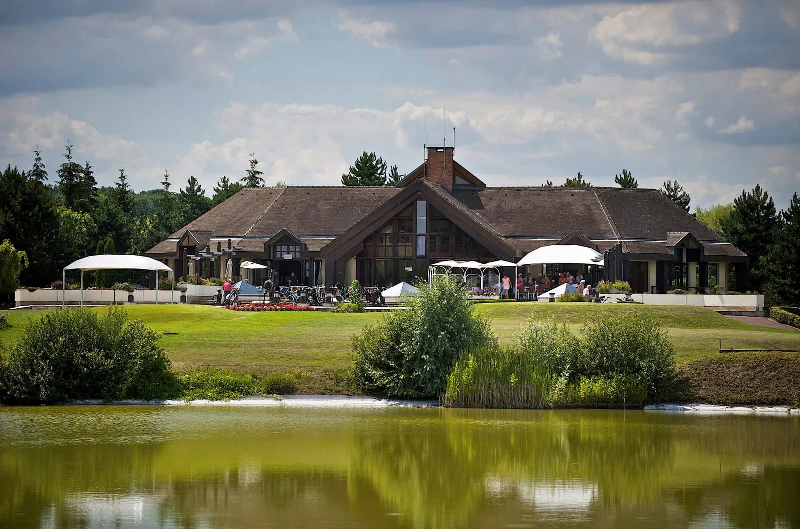 Clubhouse of the Golf Hôtel de Mont Griffon seen across its lake, with terrace parasols and a wooded backdrop