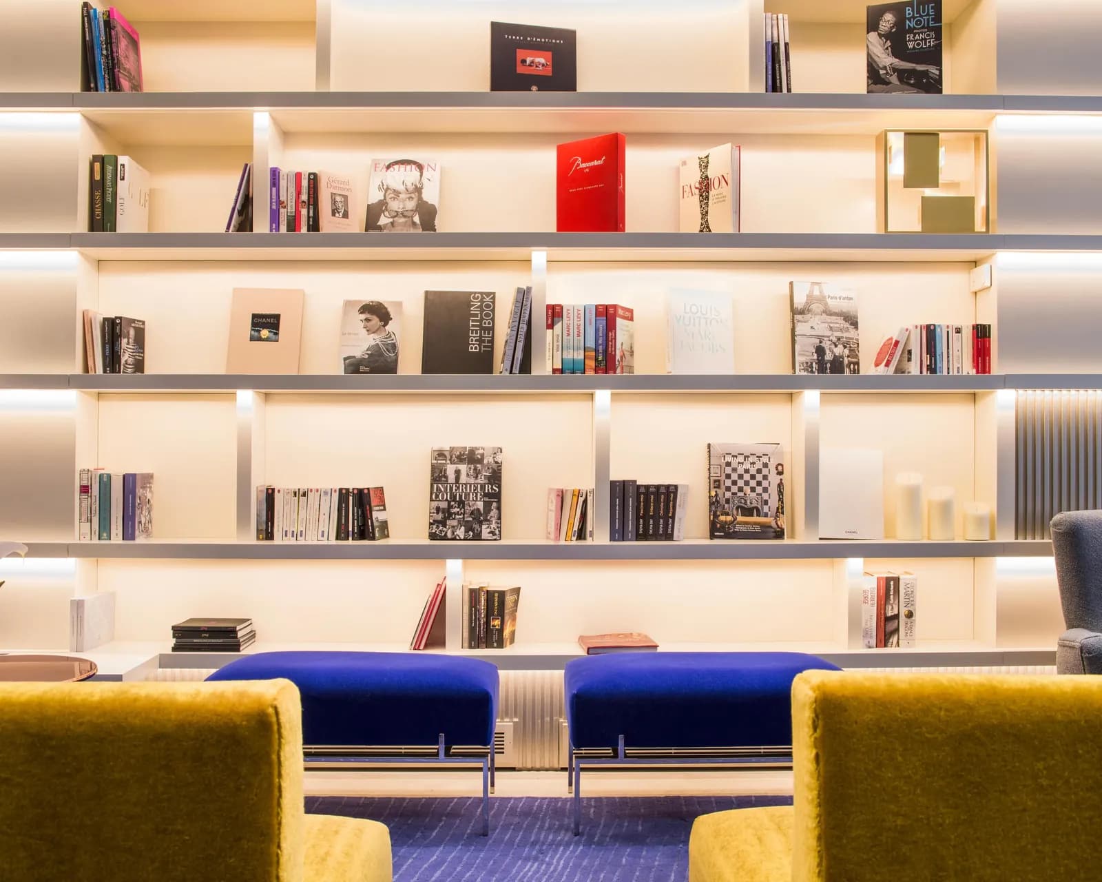 Lounge of Hôtel de Sers in Paris with a lit bookshelf wall, yellow velvet armchairs and blue ottomans