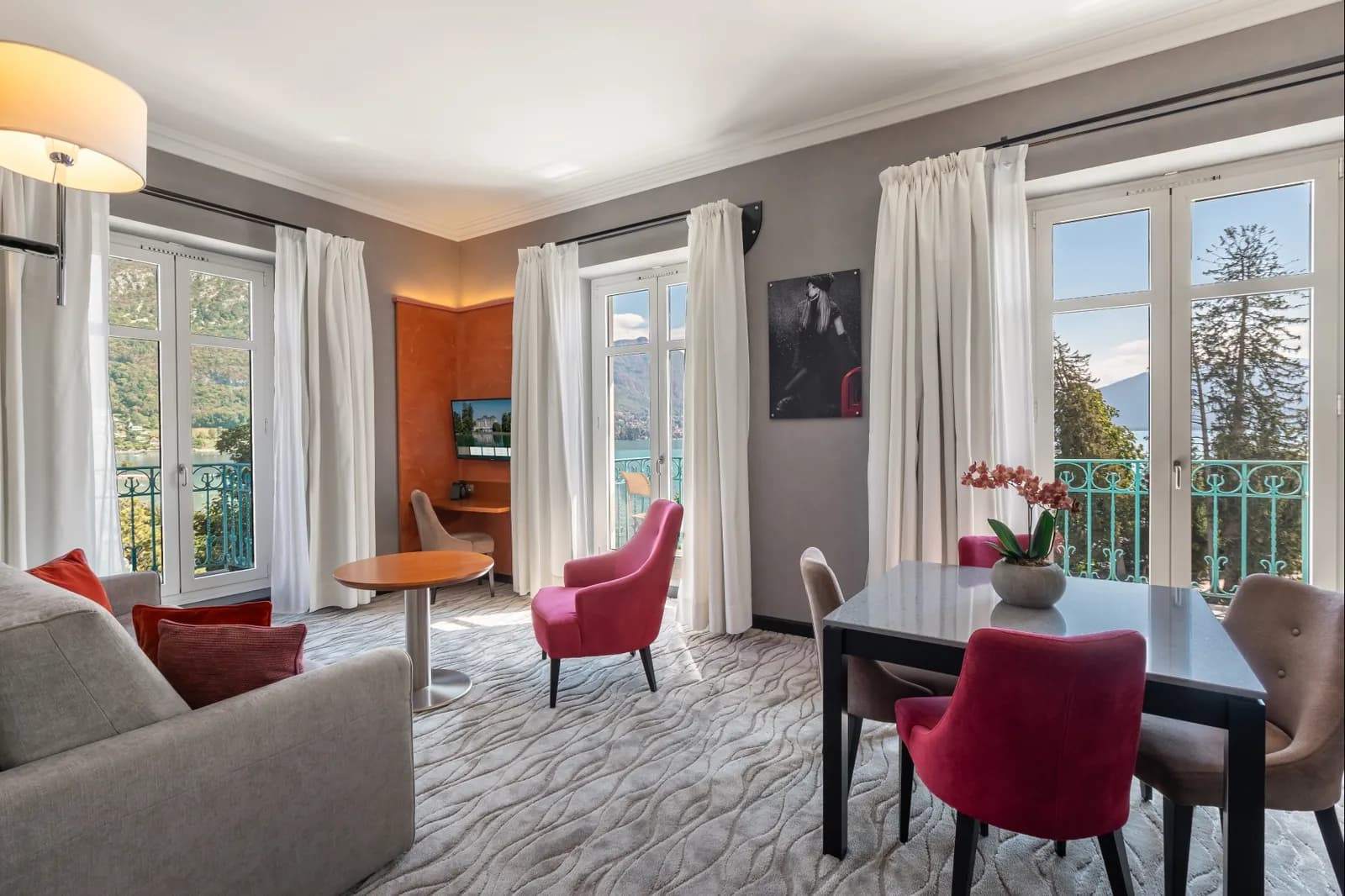Lounge area of a suite with red armchairs and lake-view balcony doors at Impérial Palace, Annecy