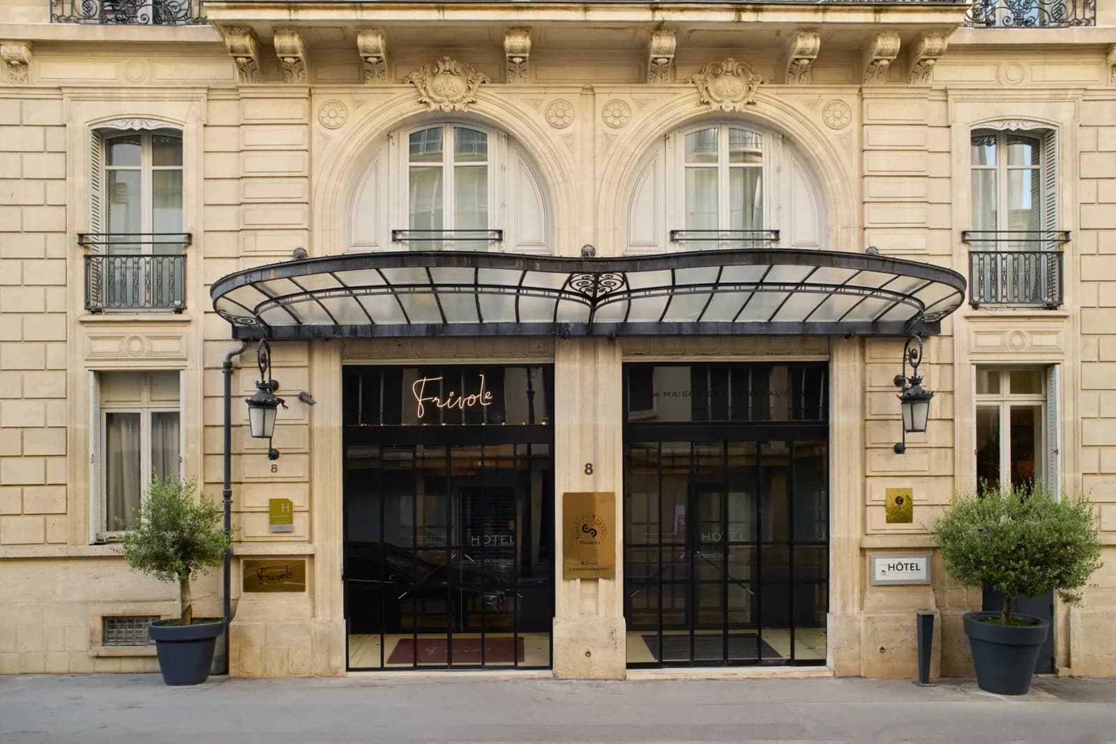 Stone facade with a glass canopy and black entrance doors at La Maison Champs-Élysées, a Design Hotel