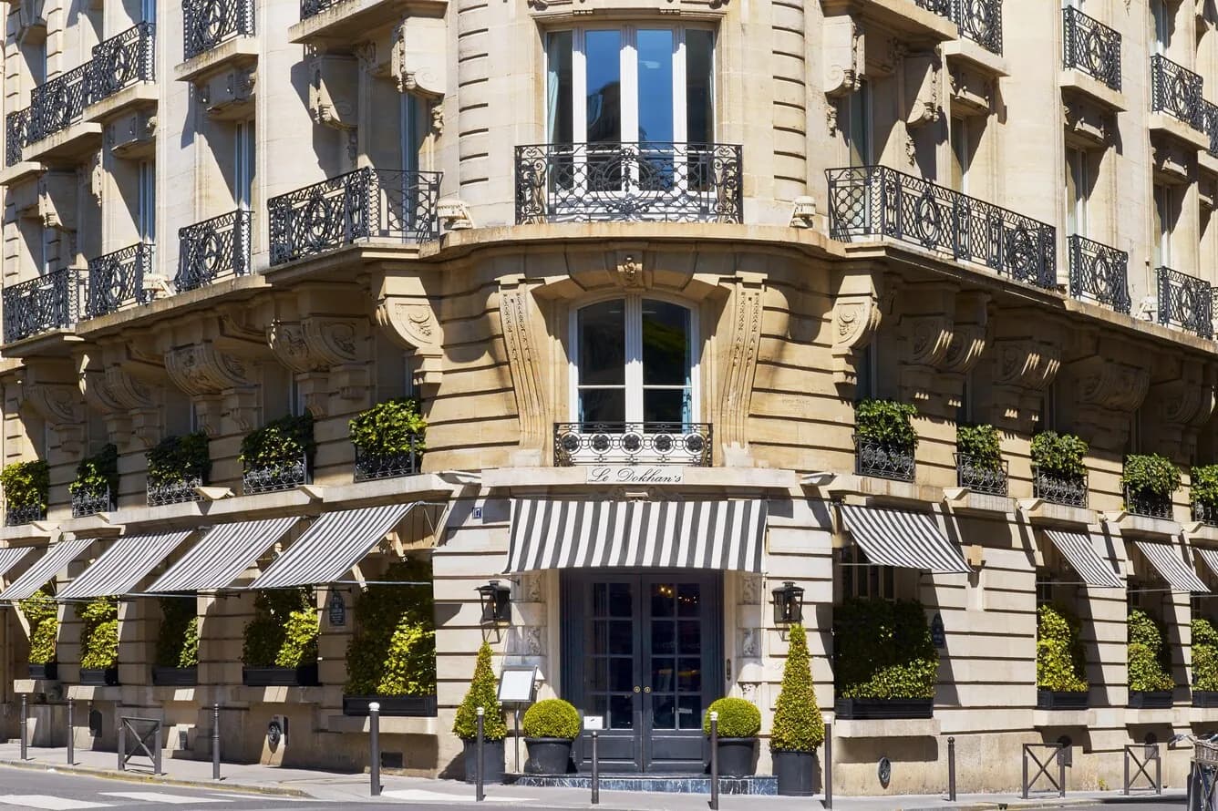 Corner façade of Le Dokhan's Paris Arc de Triomphe with striped awnings and planted balconies