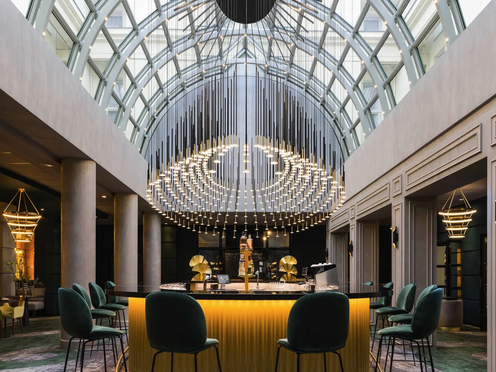 Glass-roofed atrium bar with a cascading chandelier at Le Louis Versailles Château, Versailles