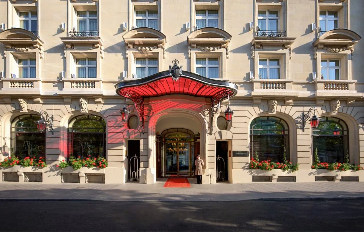 Entrance of Le Royal Monceau Raffles Paris with a red canopy and flower boxes on its stone façade
