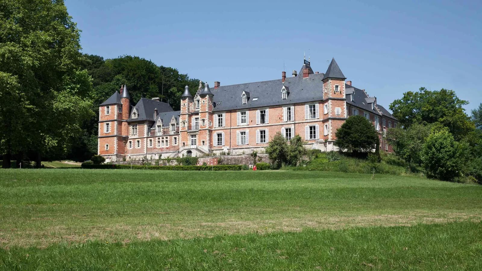 Brick and stone manor with lawns and tall trees at Manoir des Plaines Picardes, a seminar venue north of Paris