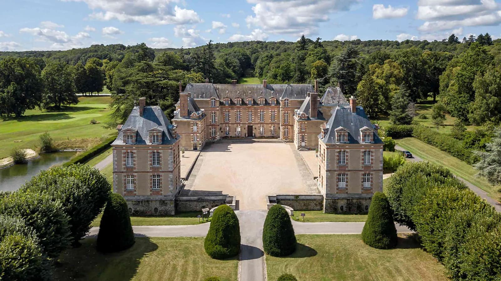 Aerial view of the manor house, its courtyard and wooded parkland at Manoir des Prés Fleuris, Yvelines