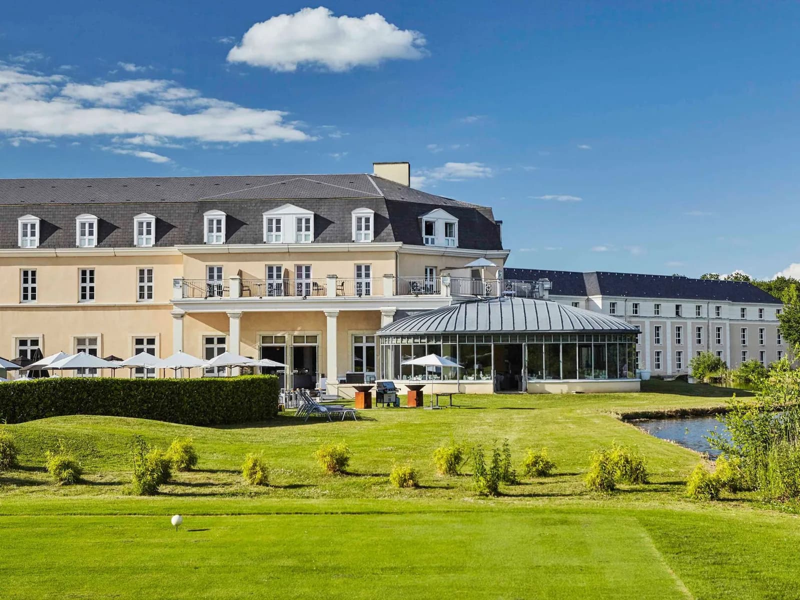 Exterior of the Mercure Chantilly Resort & Conventions, a cream-stone hotel with a glass conservatory and a lawn