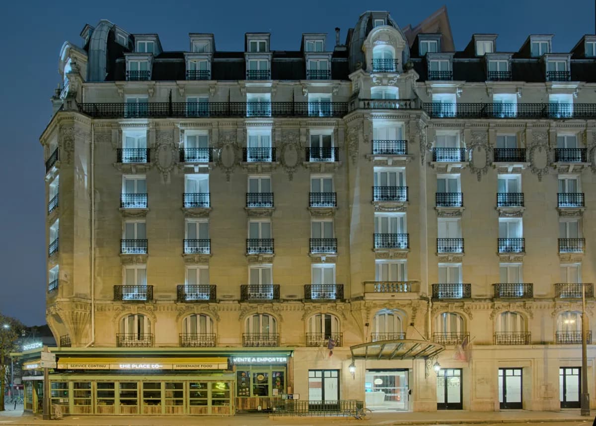 Facade of the NH Paris Gare de l'Est at dusk, a stone Haussmann-style building with lit windows and wrought-iron balconies
