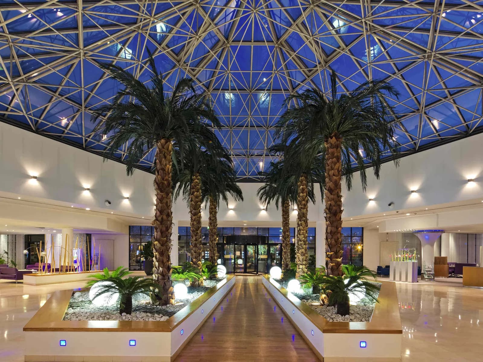 Glass-roofed atrium of the Novotel Paris Roissy CDG Convention with palm trees and a central lounge