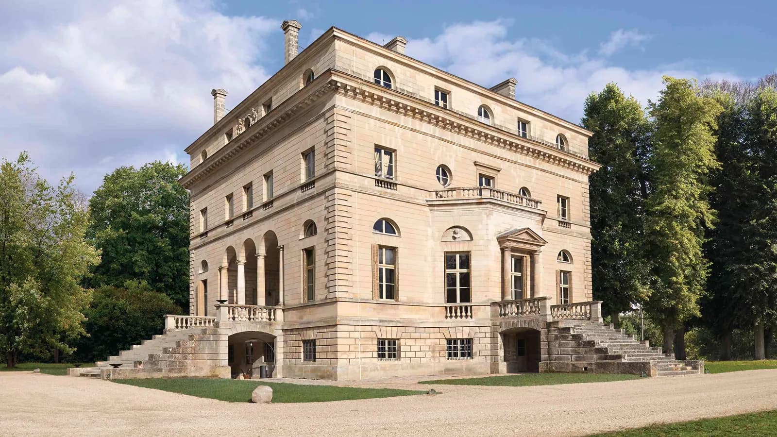 Stone palace facade with a grand staircase and tree-lined grounds at Palais des Bords d'Oise, Val-d'Oise