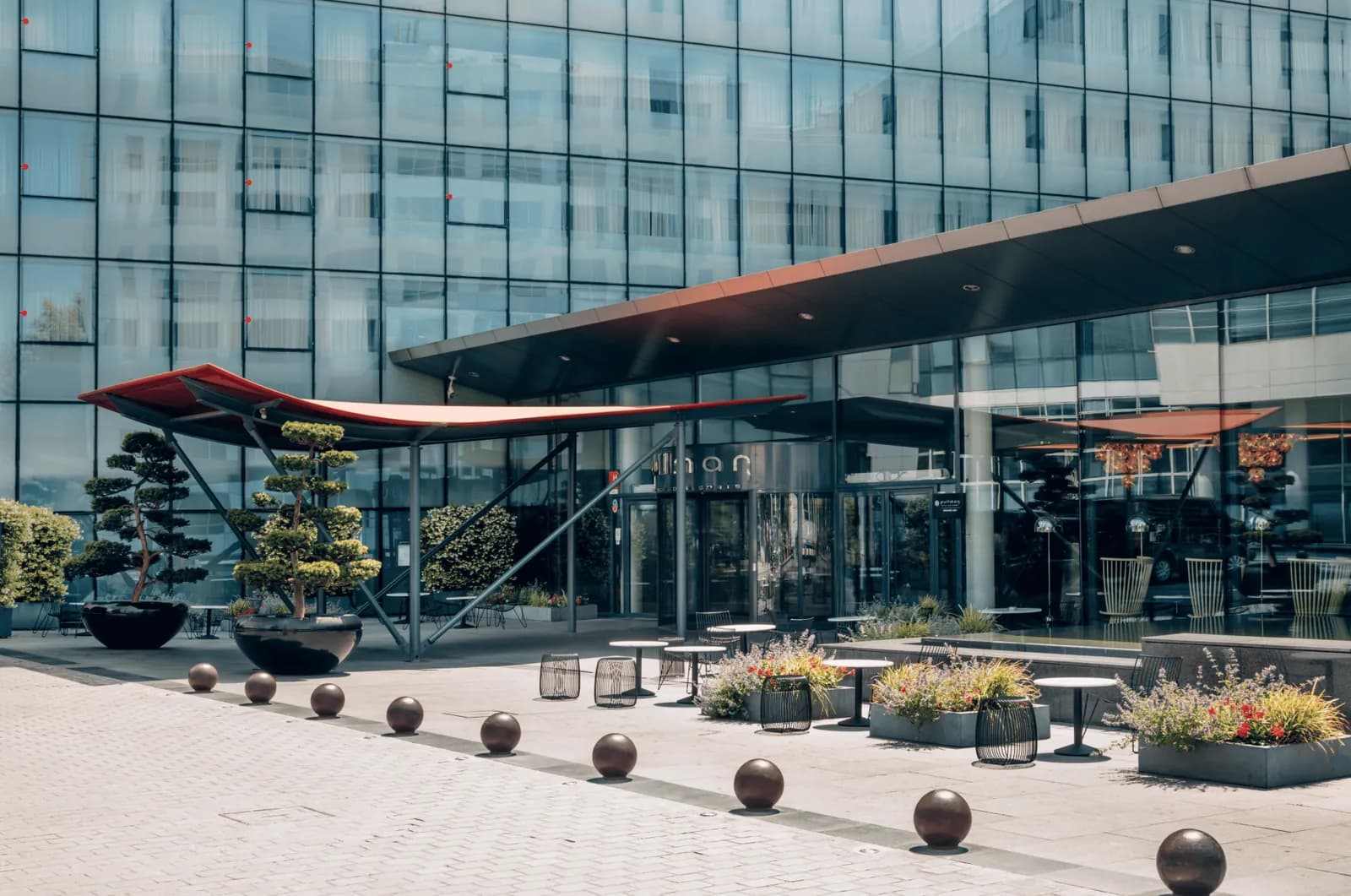 Glass facade and entrance canopy of Pullman Paris Centre-Bercy, with outdoor seating on the plaza