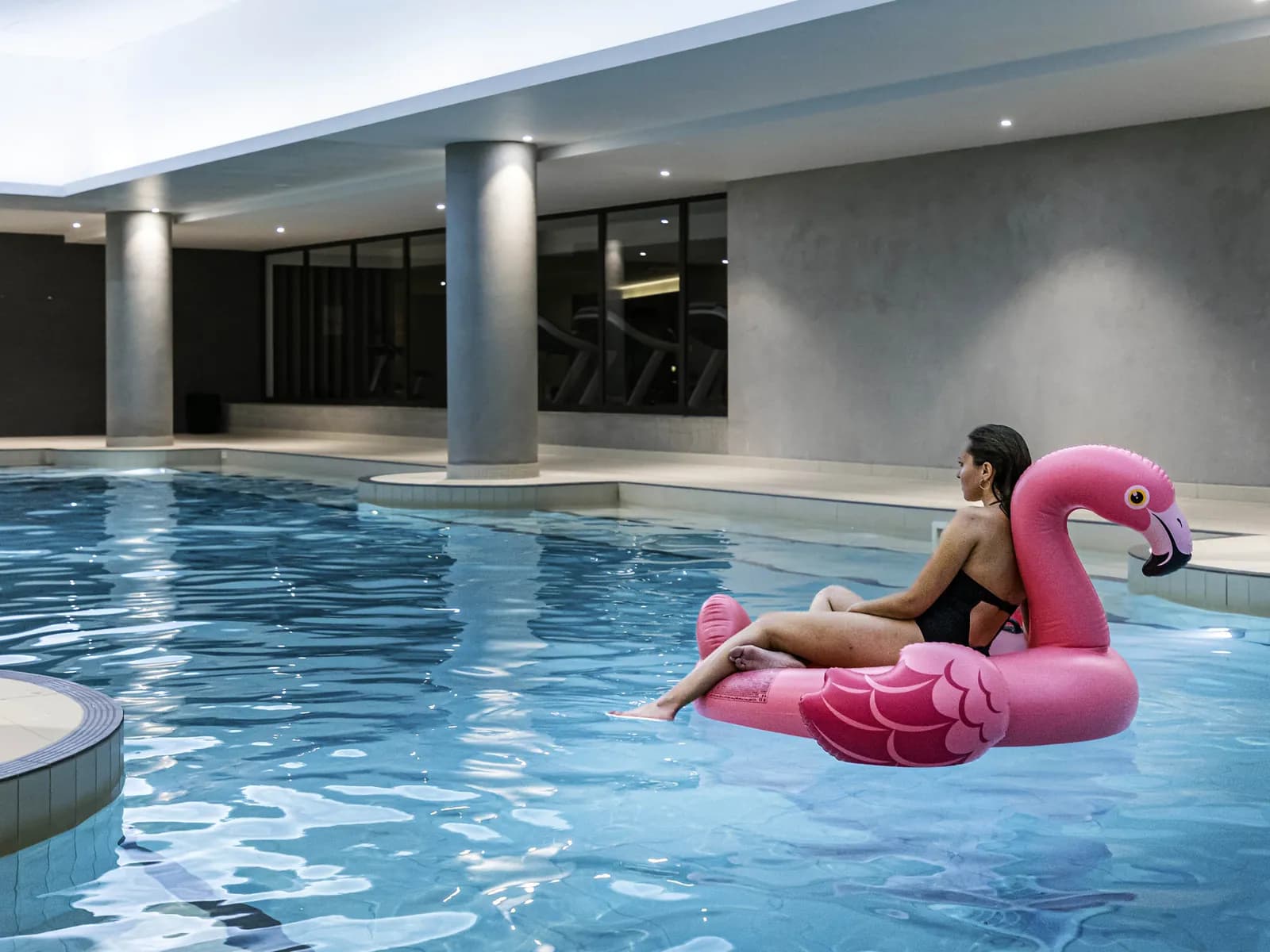 Indoor swimming pool at Pullman Paris Roissy CDG Airport with a guest floating on a pink flamingo
