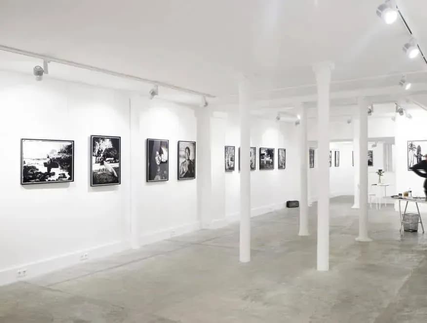 White gallery room with framed black-and-white prints on the walls and white columns