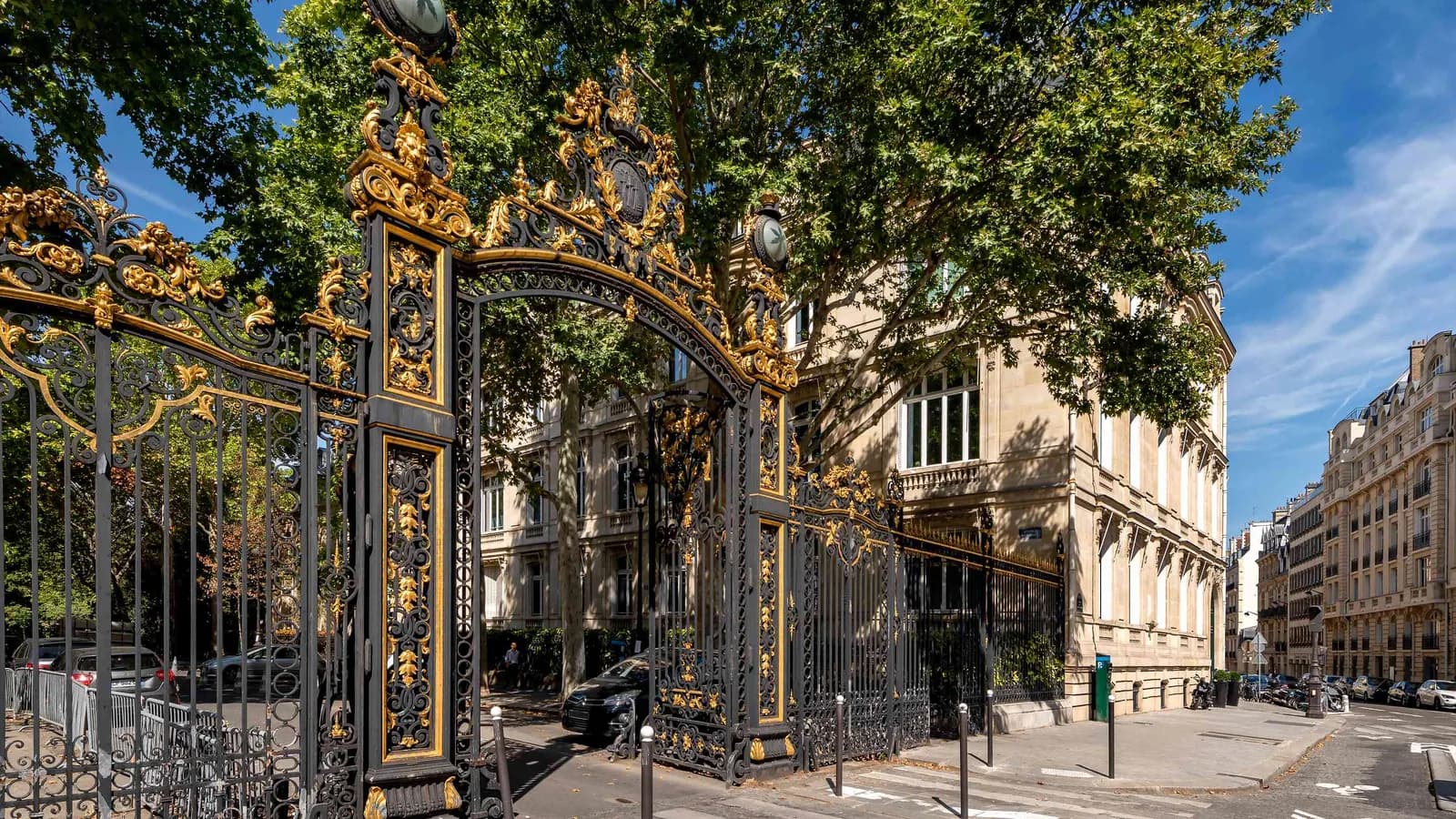 Light Atelier exterior with an ornate gold gate, a stone building and a tree-lined Paris street
