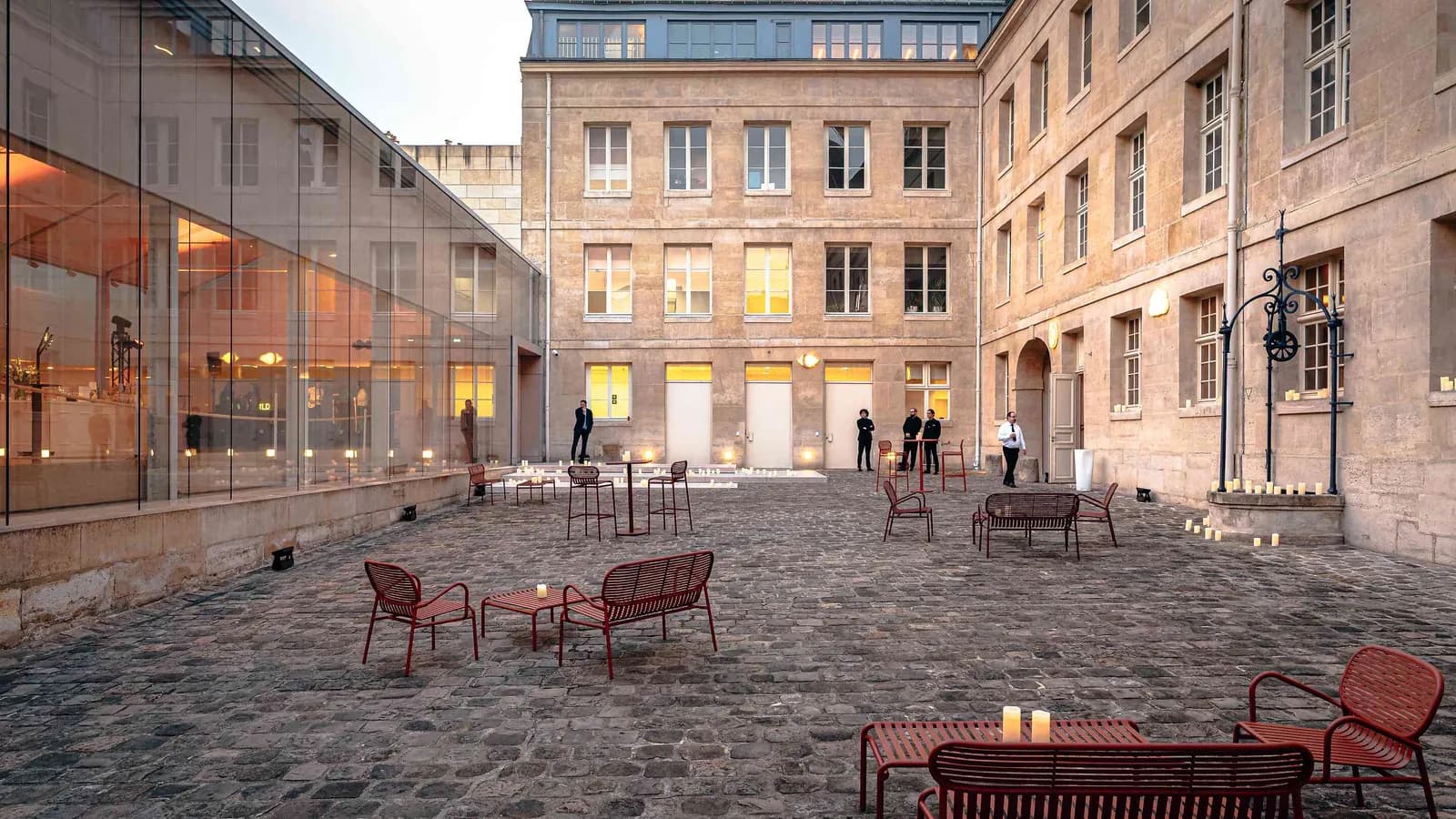 Left Bank Atrium courtyard with red garden chairs, a dusk-lit stone facade and glazed hall