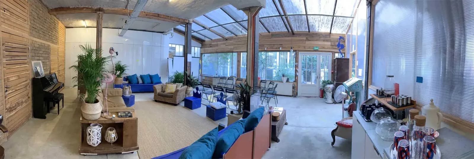 Panoramic studio with a glass roof, lounge seating with blue cushions, a piano and wooden wall panels