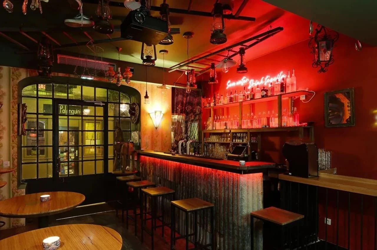 Bar with a red neon sign, a corrugated metal counter and high stools.