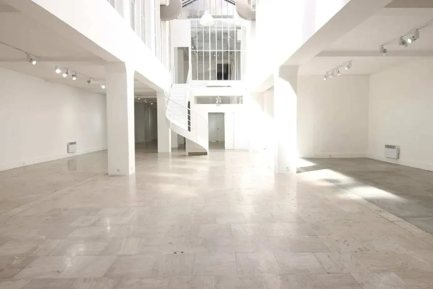 White hall with a curved staircase, tall columns and a skylit ceiling