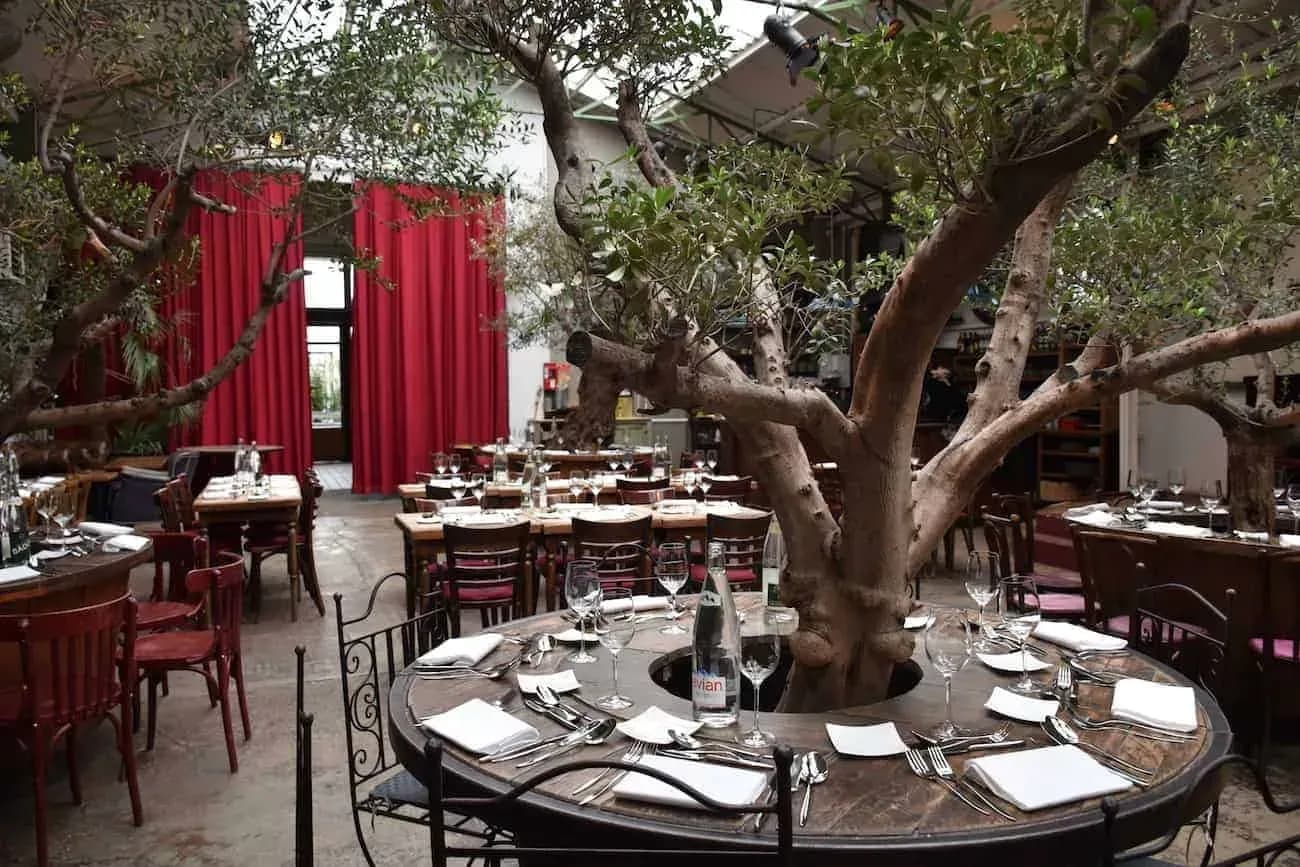 Industrial hall with a glass roof, olive trees and round dining tables