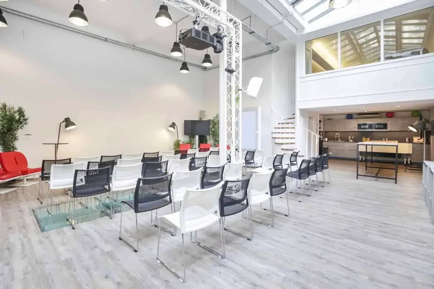Bright room under a glass roof set with rows of chairs facing a presentation area