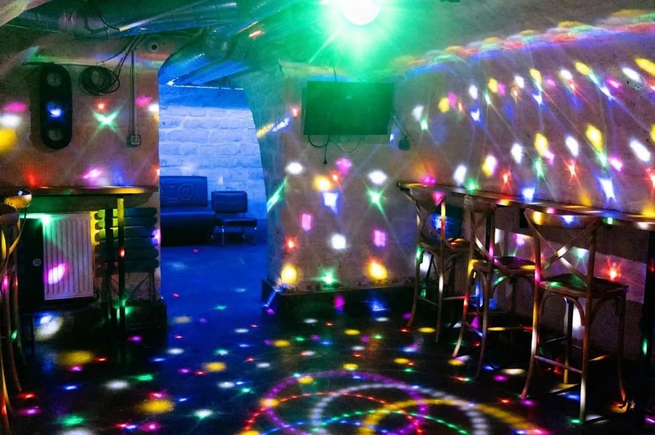 Cellar room with coloured stage lighting, bar stools and stone walls.