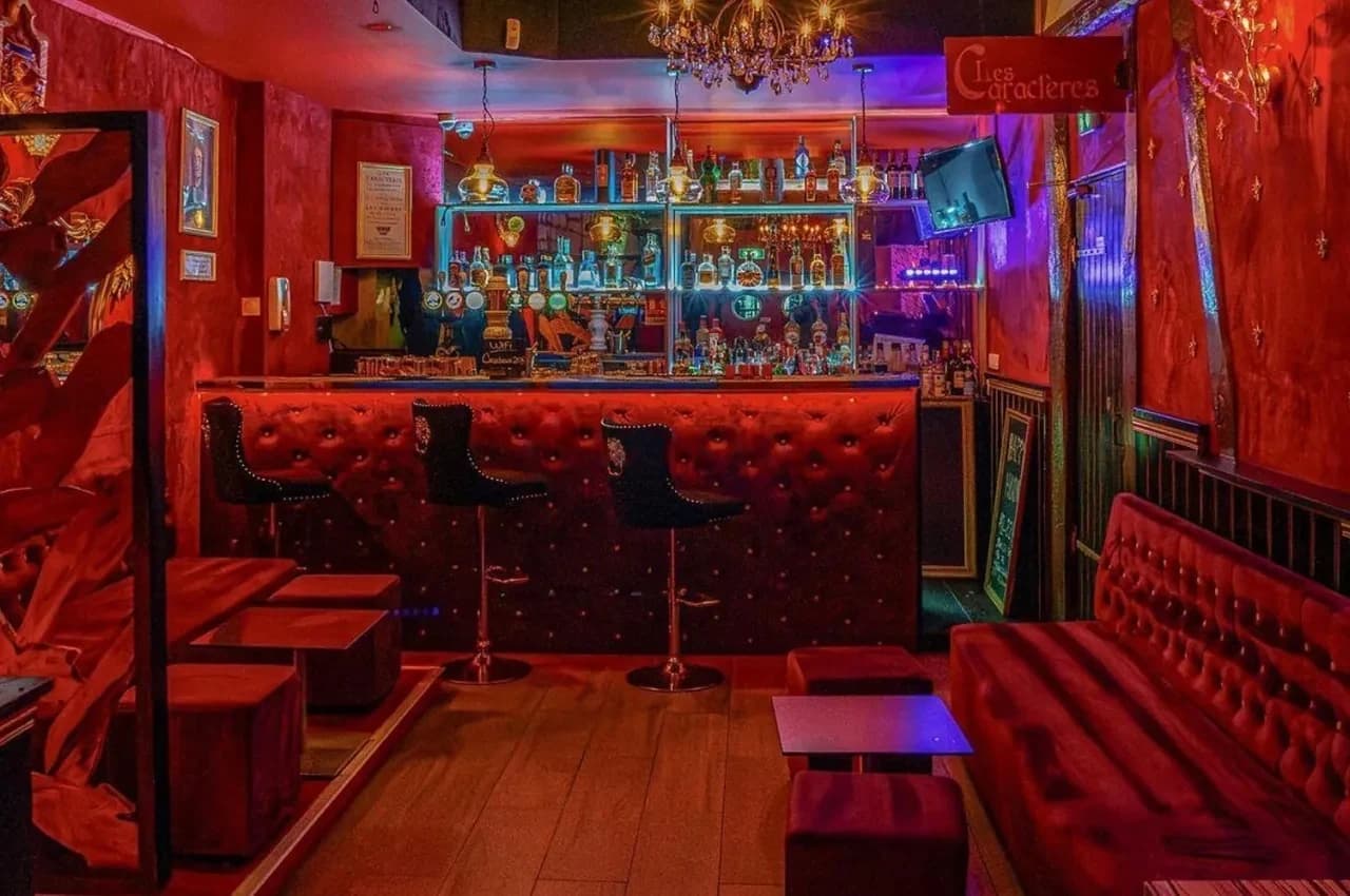 Bar with red velvet banquettes, a chandelier and illuminated bottle shelves.