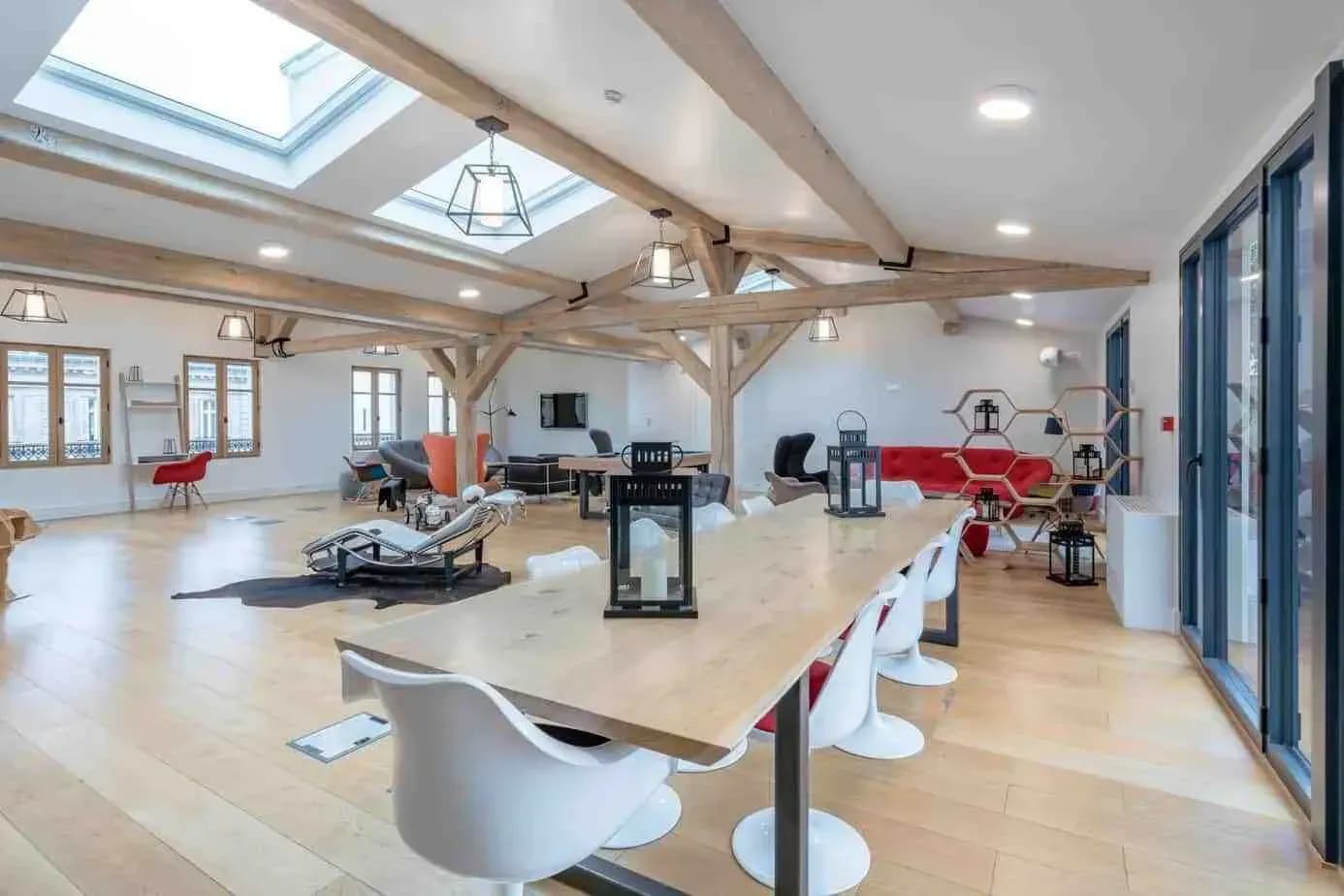 Loft-style penthouse room with exposed timber beams, skylights and a long wooden table with white chairs