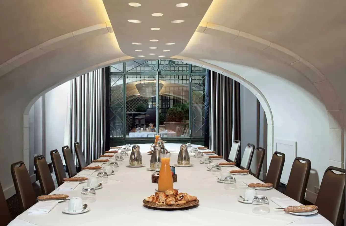 Vaulted salon with a long table set for a meeting and tall windows