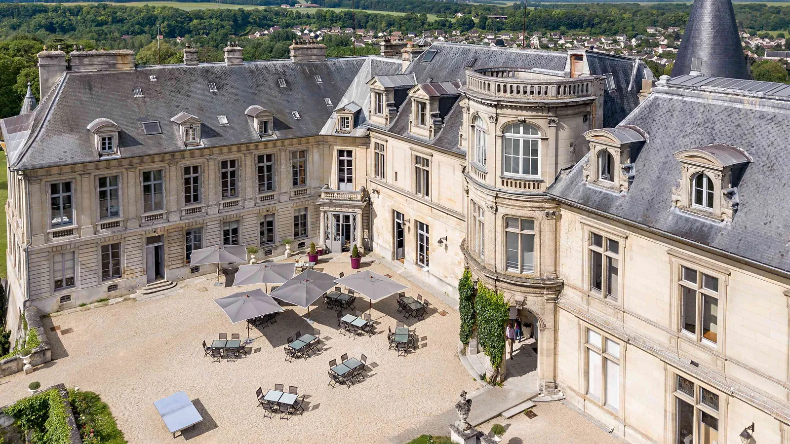 Courtyard of Château des Tourelles Blanches with a round tower, dormer windows and parasols