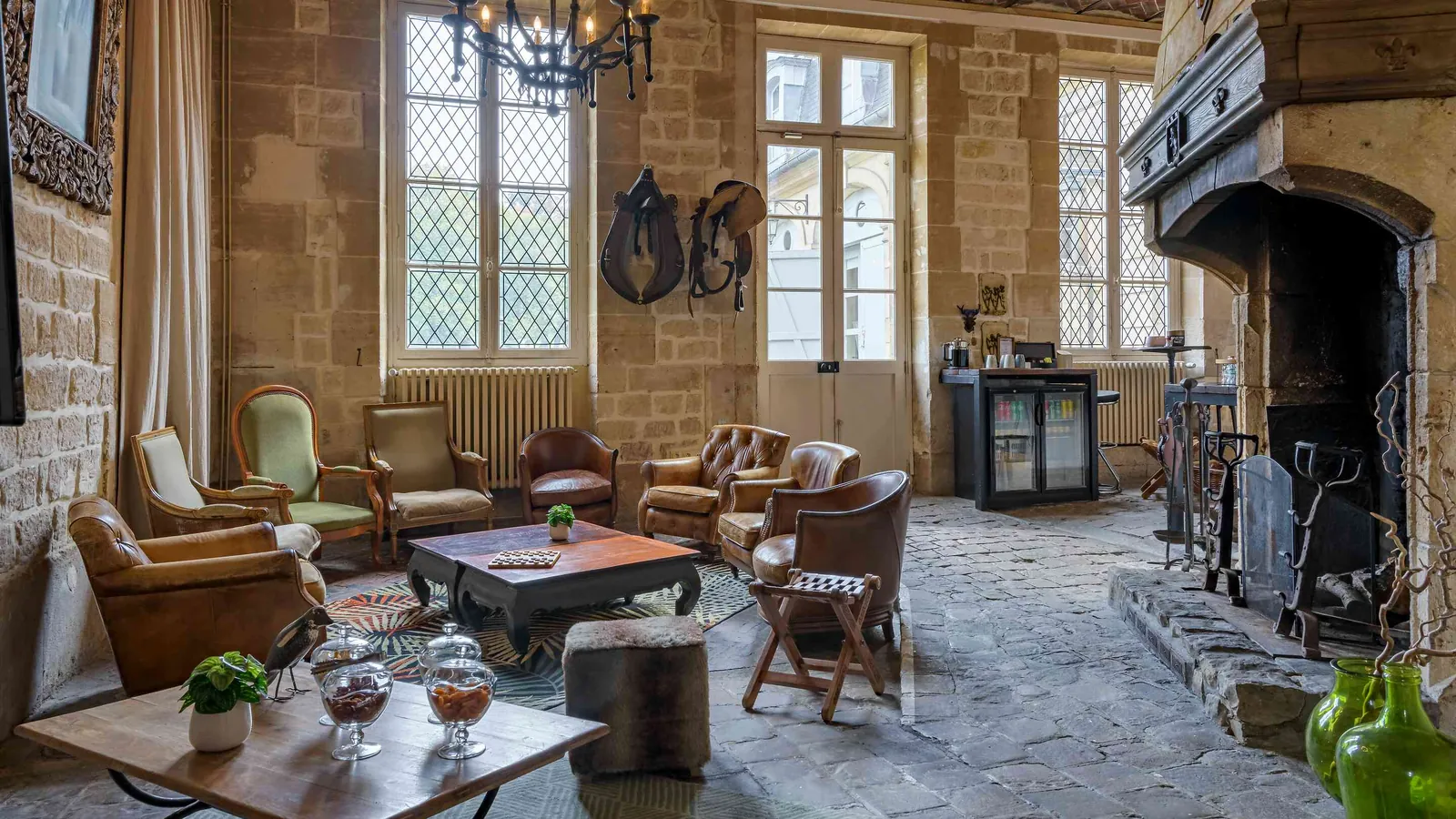 Stone-walled lounge with a large fireplace, leather armchairs and a low table at Château du Val Vert