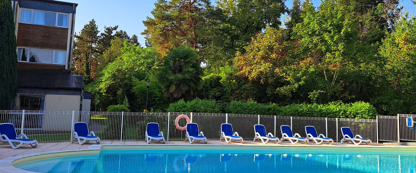 Illuminated pool beside loungers at dusk at Domaine des Rives de l'Orge, a wooded seminar resort in Essonne