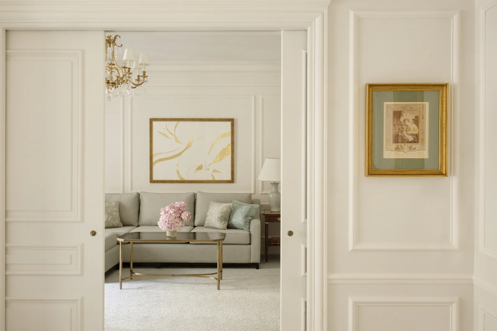 Suite sitting room with a cream sofa, gilded artwork and panelled doors at Four Seasons Hotel George V, Paris