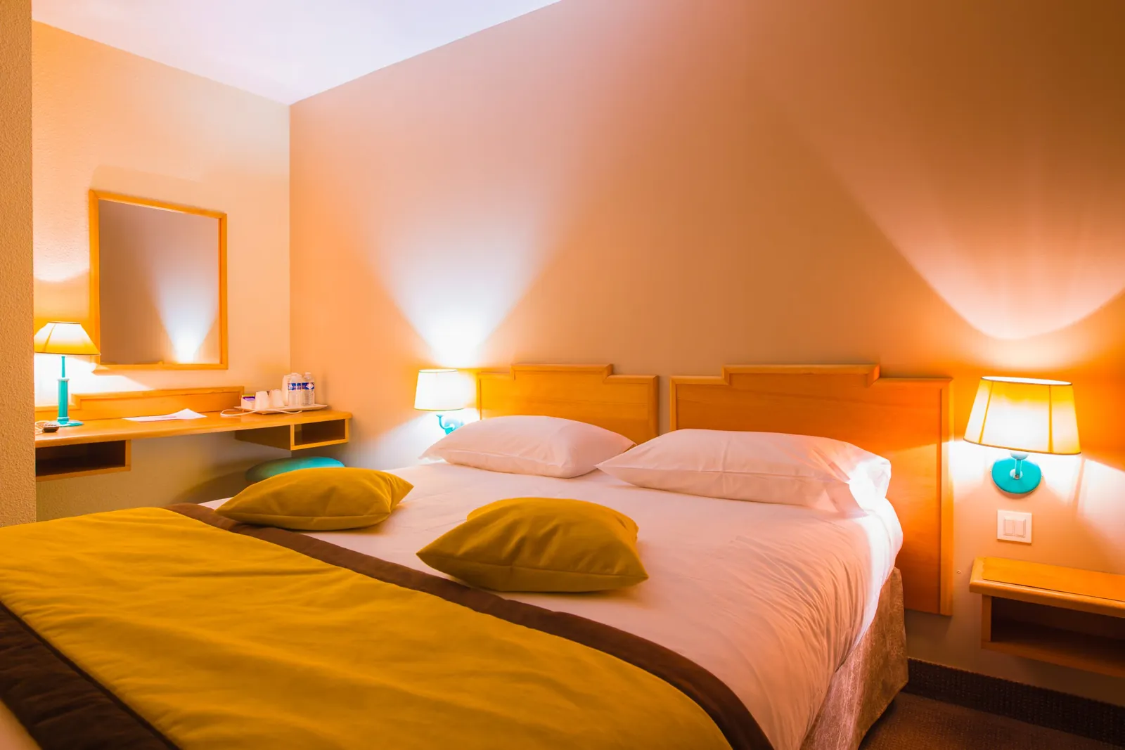 Double guest room at the Golf Hôtel de Mont Griffon with orange accents, a warm bedside lamp and a writing desk