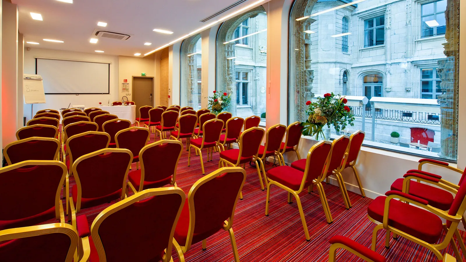 Meeting room set classroom-style with red chairs and tall windows at Hôtel de Bourgtheroulde, Rouen