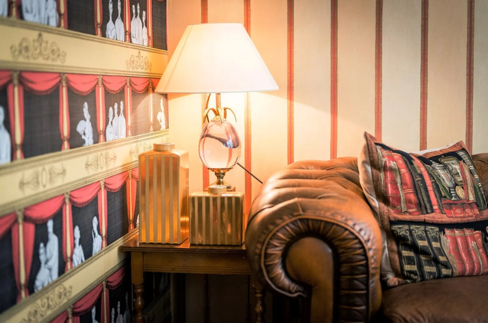 Library lounge of Hôtel du Théâtre with striped theatre wallpaper, a brown leather sofa and a table lamp