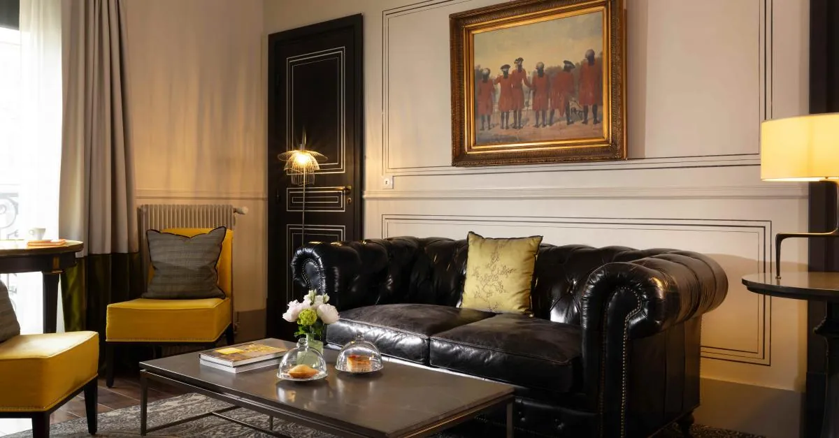 Lounge with black leather Chesterfield sofa, yellow armchairs and framed painting at Hôtel Edouard VII, Paris