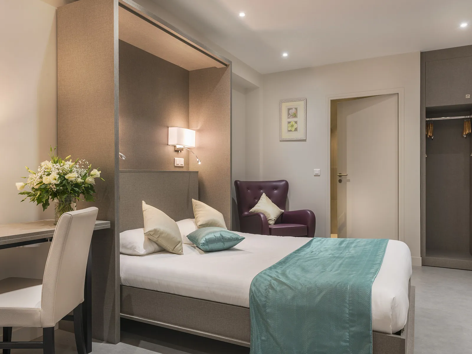 Double bedroom at Hôtel France Albion with a teal throw, white flowers on a desk and a plum armchair