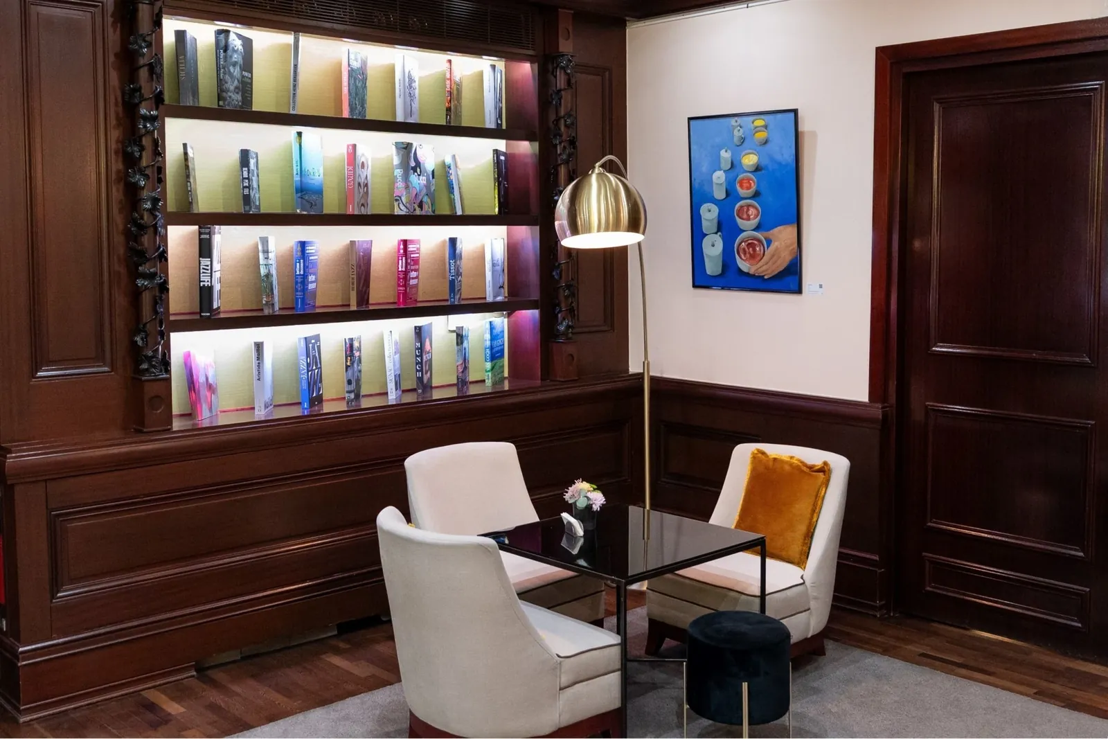 Library lounge at Hôtel Pont-Royal in Paris with lit bookshelves, cream armchairs and a wooden wall