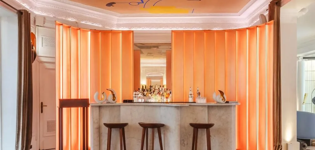 Bar of Hôtel Vernet in Paris with orange curtains, a stone counter and tall wooden stools